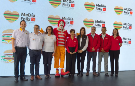 Grupo de colaboradores junto a Ronald McDonald durante un evento del McDía Feliz, con logotipos de la campaña al fondo.