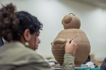 Persona dando forma con una herramienta a una escultura de arcilla en un taller de cerámica.